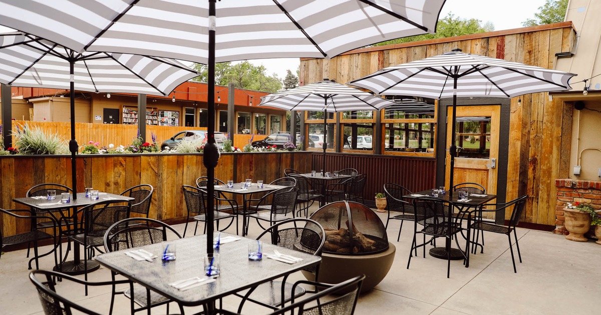 Outdoor dining area with striped umbrellas, string lights, and a modern fire pit
