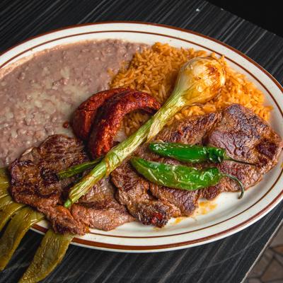 Grilled steak with rice, beans, green onion, and peppers on a plate.