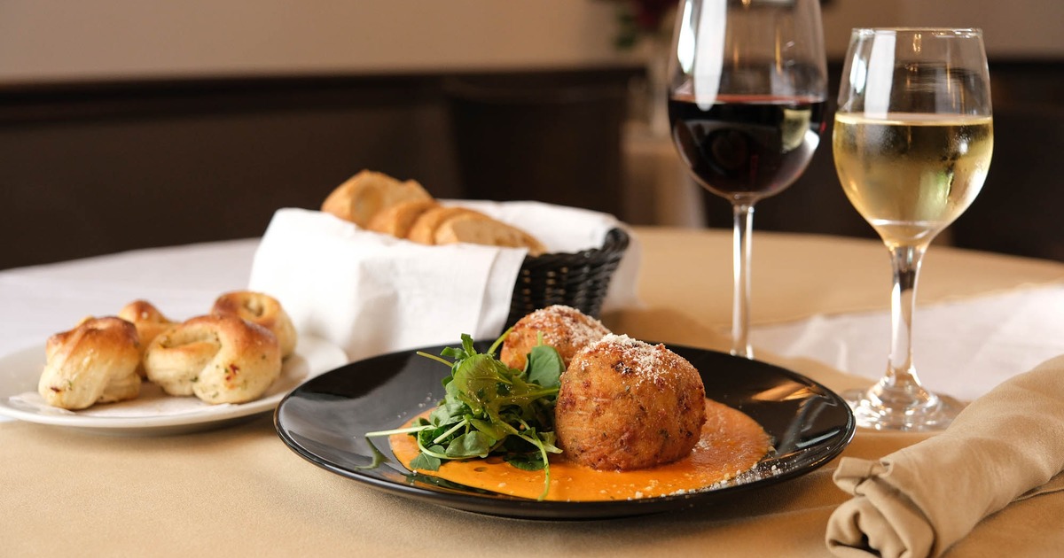 A plate of fried arancini with sauce and greens, accompanied with garlic knots, bread, and wine