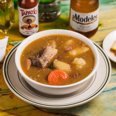 Bowl of meat and root vegetable stew served alongsid a bottle of beer.