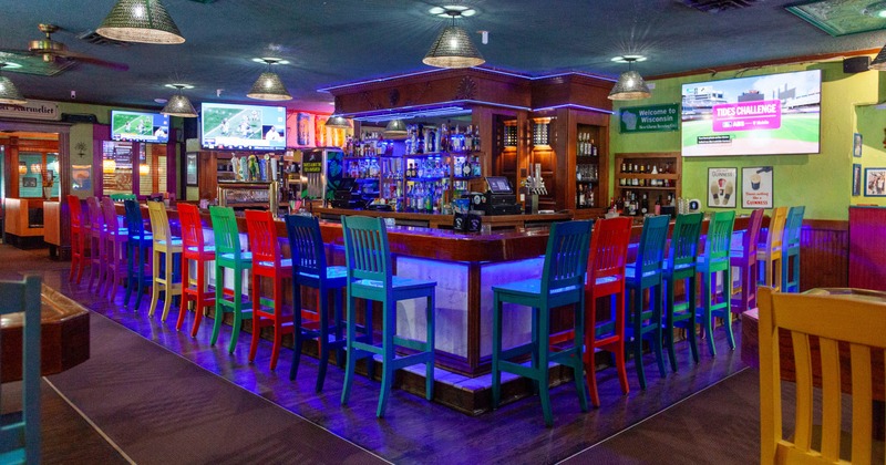 Interior, bar area, massive wooden top bar with colorful wooden stools, large drink shelf
