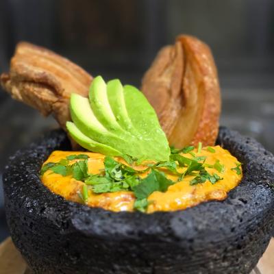 Spicy dish in a stone mortar, topped with avocado slices, cilantro, and crispy pork.