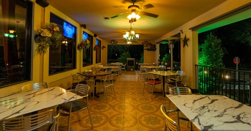 Outdoor restaurant patio at night with marble-top tables, metal chairs, decorative flowers