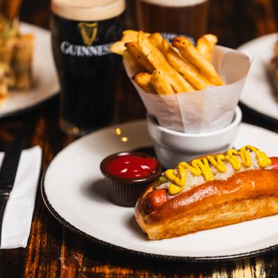 Hot dog topped with coleslaw and mustard, served with fries, ketchup, and a pint of stout.