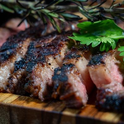 Sliced grilled steak with herbs and rosemary on a wooden cutting board.