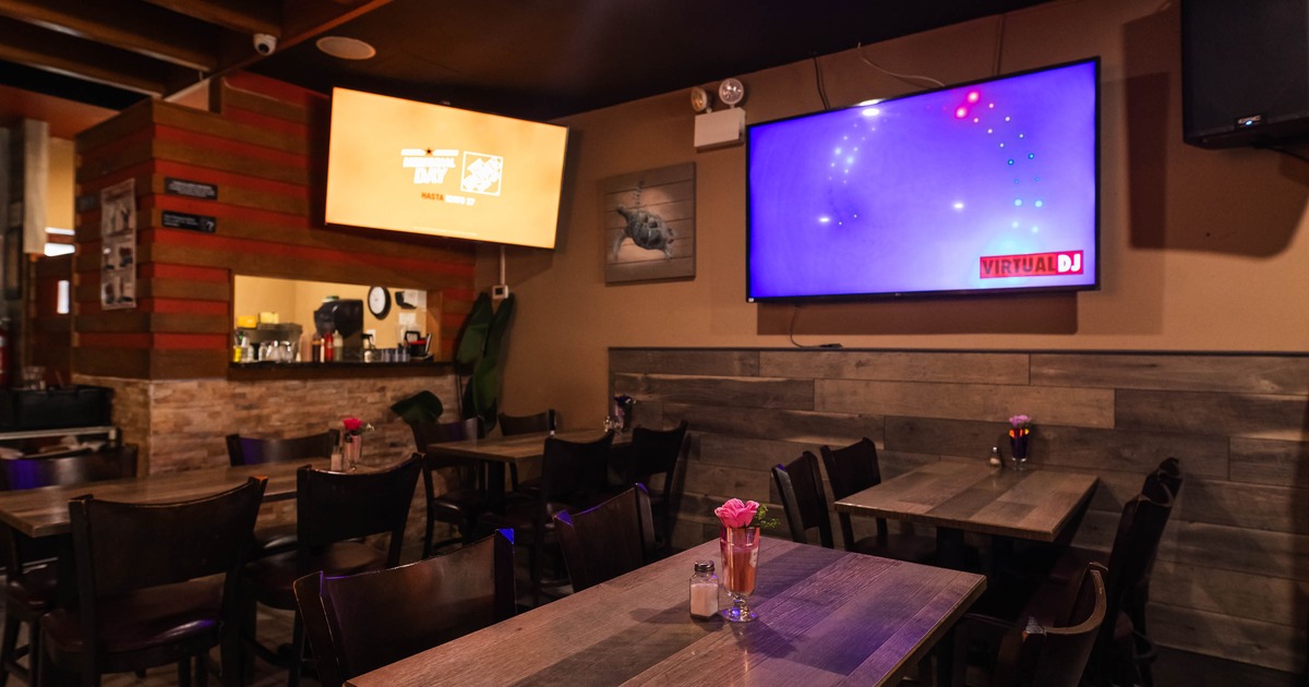 Interior of a restaurant with wooden tables and chairs, TV screens, and ambient lighting