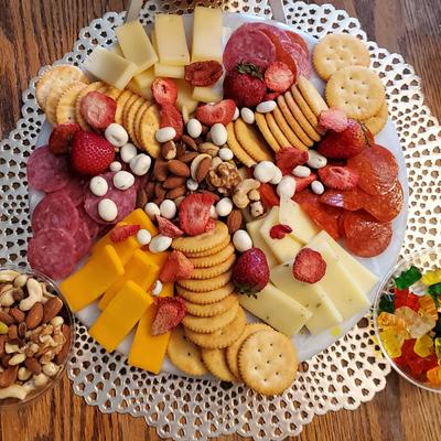 A colorful charcuterie board with bowls of mixed nuts and gummy bears on the side.