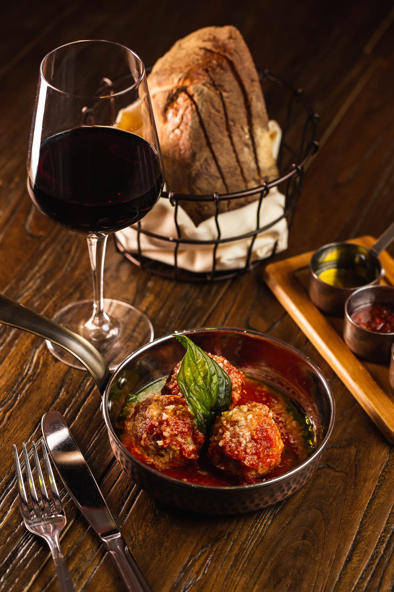 Meatballs and a glass of red wine, bread, and condiments on a table