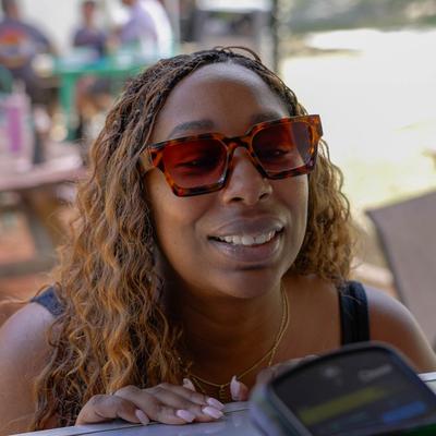 A smiling person wearing sunglasses making a purchase outdoors.