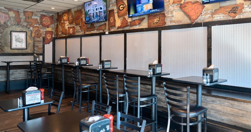 Casual dining area with high tables and chairs, decorated with sports team plaques and three TVs