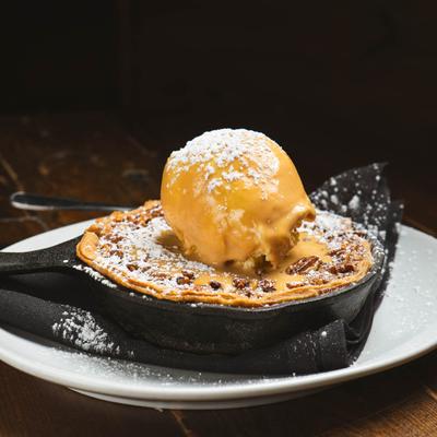 Pecan pie in a skillet with a scoop of buttermilk ice cream.