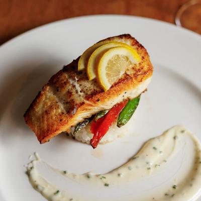 Seared salmon served over rice and peppers with a sauce smear on a plate