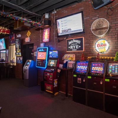 Several gaming machines lined up against the wall, alongside neon signs.