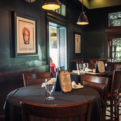 Restaurant interior with dark walls and decor, set tables, and wall art.