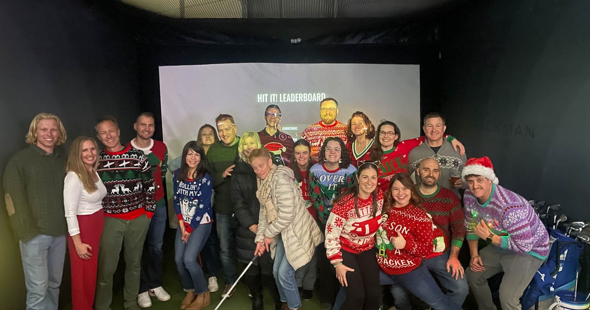 A group of people posing for the shot in front of a golf simulator screen