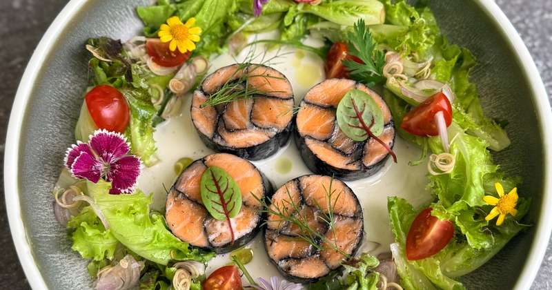 Salmon mosaic served in a sauce with fresh greens,cherry tomatoes and edible flowers