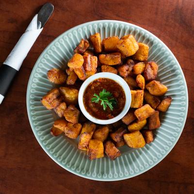 A plate of fried plantain bites, served on a plate with a cup of dipping sauce.