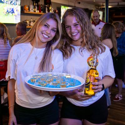 Two people holding a tray and a bottle.