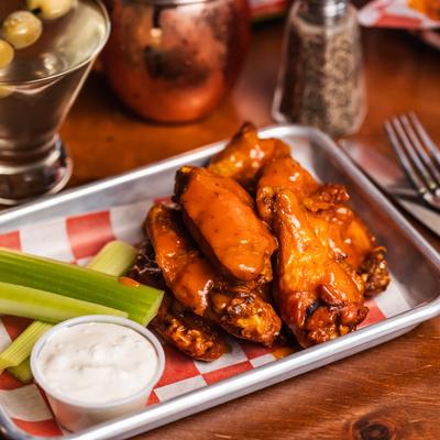 Plate of spicy buffalo wings with celery sticks and ranch dip on red-checked paper.