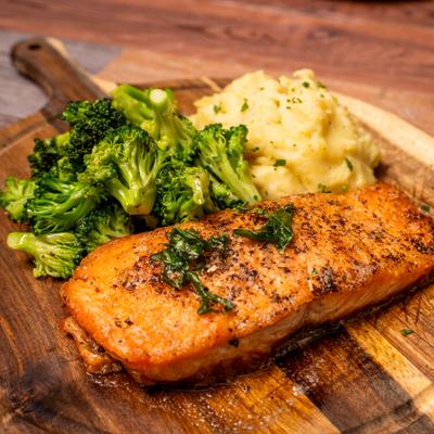 Seared salmon served with broccoli and mashed potatoes on a wooden board.