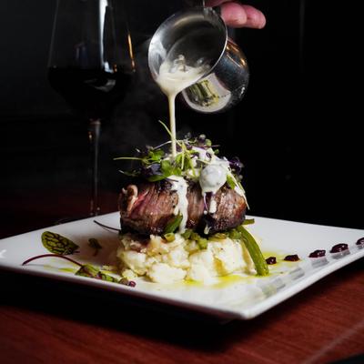 Sirloin steak on a bed of mashed potatoes being topped with a creamy sauce.