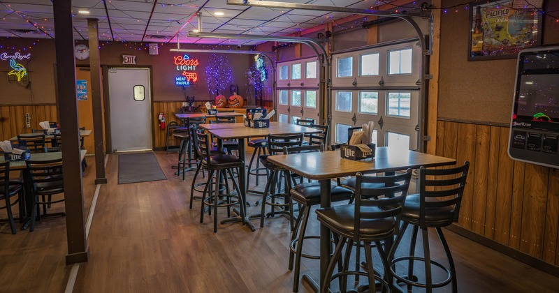 Casual dining area with wooden tables and stools, neon signs, string lights