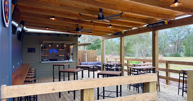 Covered patio with heaters, ceiling fans, and tall wooden tables near the outdoor bar