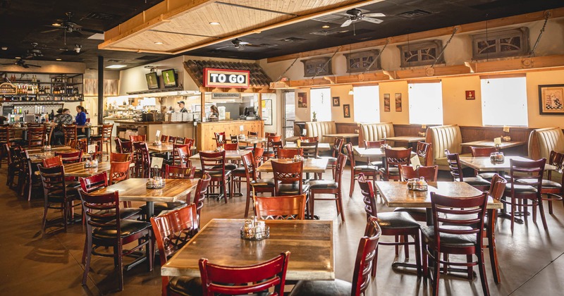 Interior, dining area, wooden top tables with chairs, kitchen and bar in the back
