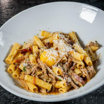 Ziti pasta topped with a raw egg yolk, grated cheese, and a rich, savory meat sauce.