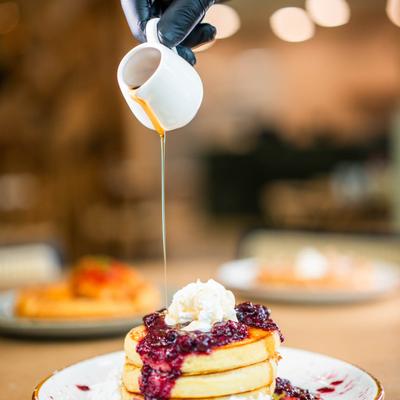 Fluffy pancakes topped with berry compote, whipped cream, and drizzled with syrup.