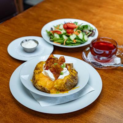 A loaded baked potato with bacon and sour cream accompanied by a salad and a cup of tea.