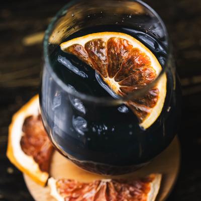 Dark cocktail drink garnished with dry citrus slices.