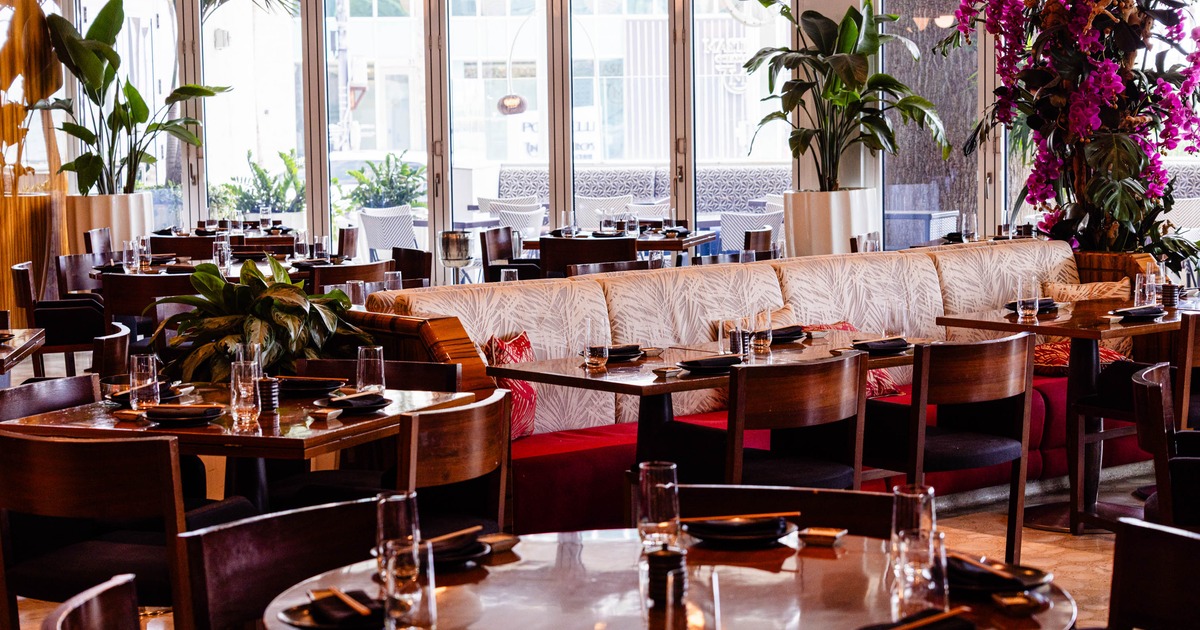 An elegant interior - wooden tables & chairs, a cushioned leaf-patterned bench and large windows