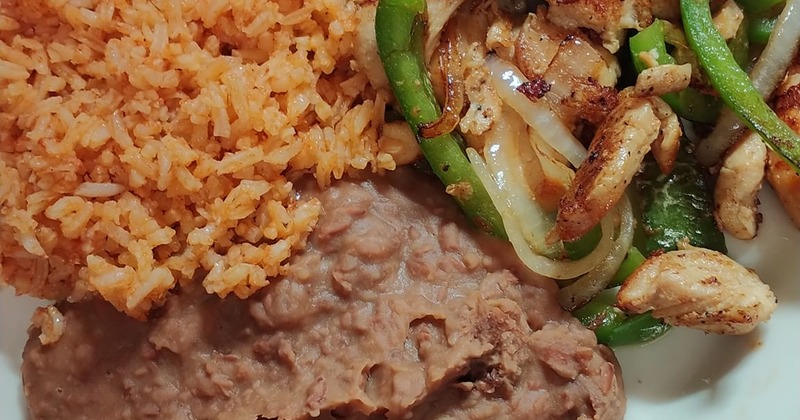 A plate of chicken fajitas served with Mexican rice and refried beans
