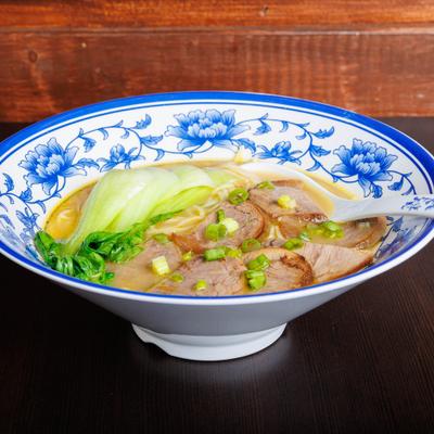 Beef noodle soup with bok choy and scallions in a blue floral bowl.