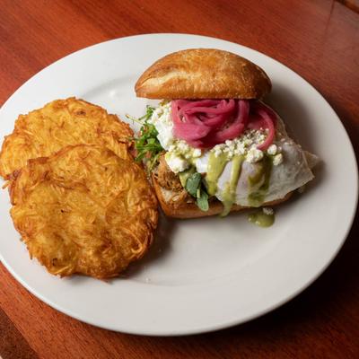Pork sandwich with eggs, arugula, pickled red onion, poblano sauce, cheese, and hash browns.