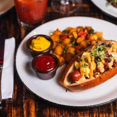 Breakfast hot dog with eggs and potatoes on a white plate.