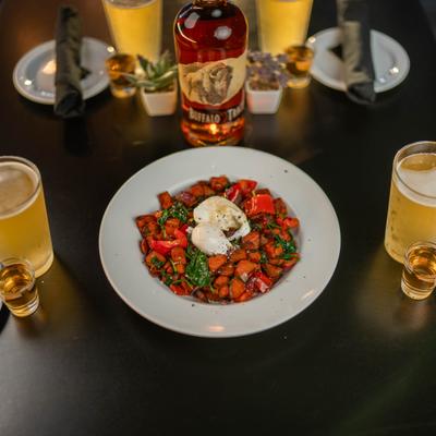 Sweet potato hash browns topped with poached eggs, accompanied by beers and bourbon shots.