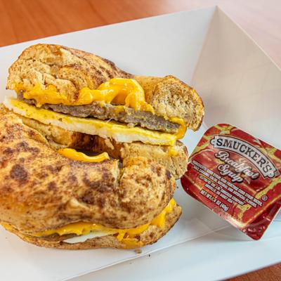 A sausage, egg, and cheese bagel sandwich, served with branded breakfast syrup.