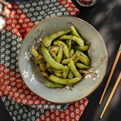 A bowl of seasoned edamame pods sits next to wooden chopsticks.