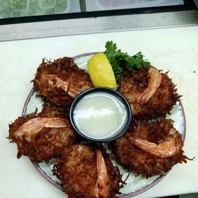 Coconut shrimp plate with a sauce dip in the middle, lemon wedge and cilantro garnish.