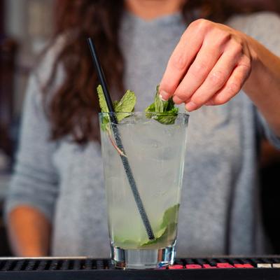 Bartender garnishing a Mojito cocktail glass with mint leaves.