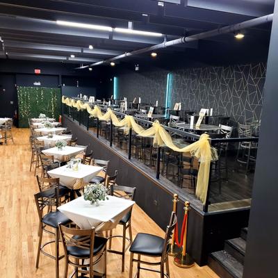 Event setup with arranged dining tables and a raised platform aera with decorative draping.