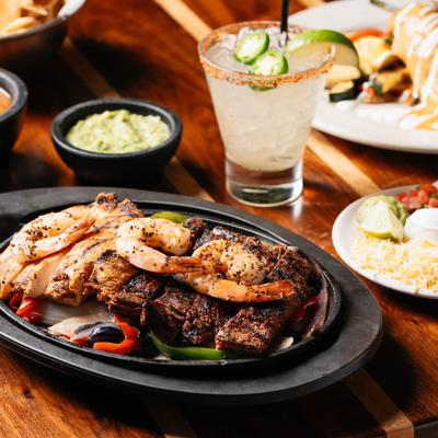 Mixed fajita plate with a Jalapeno Margarita and assorted dishes on a table.