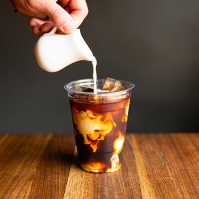 a glass of cold brewed coffee as creamer is being poured into it.