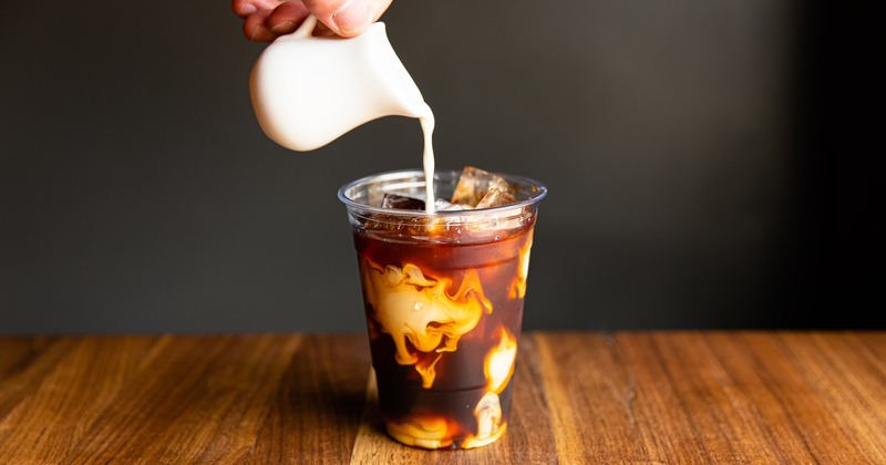 a glass of cold brewed coffee as creamer is being poured into it