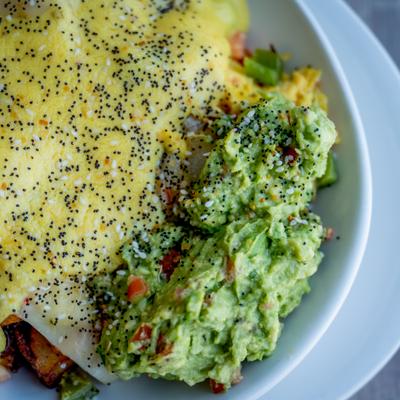 Smashed avocado bowl with scrambled eggs, melted cheese, and poppy seeds.
