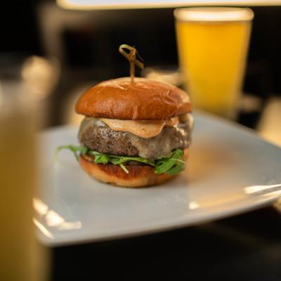 Juicy burger on a toasted bun with melted cheese, arugula, and creamy orange sauce.