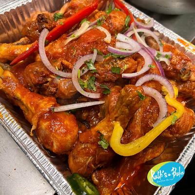Spicy chicken drumsticks garnished with onions and peppers in a foil tray.