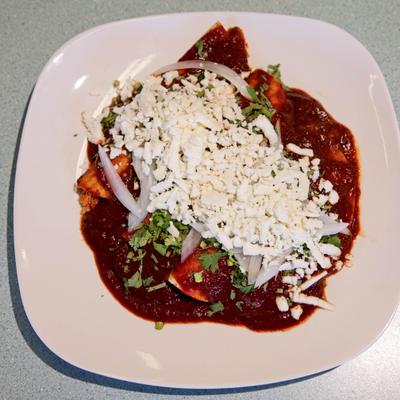 Enchiladas Rojas topped with crumbled queso fresco, cilantro and sliced onion.
